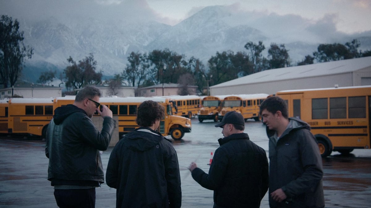 The production team is engaged in a discussion amidst a location filled with numerous parked yellow school buses