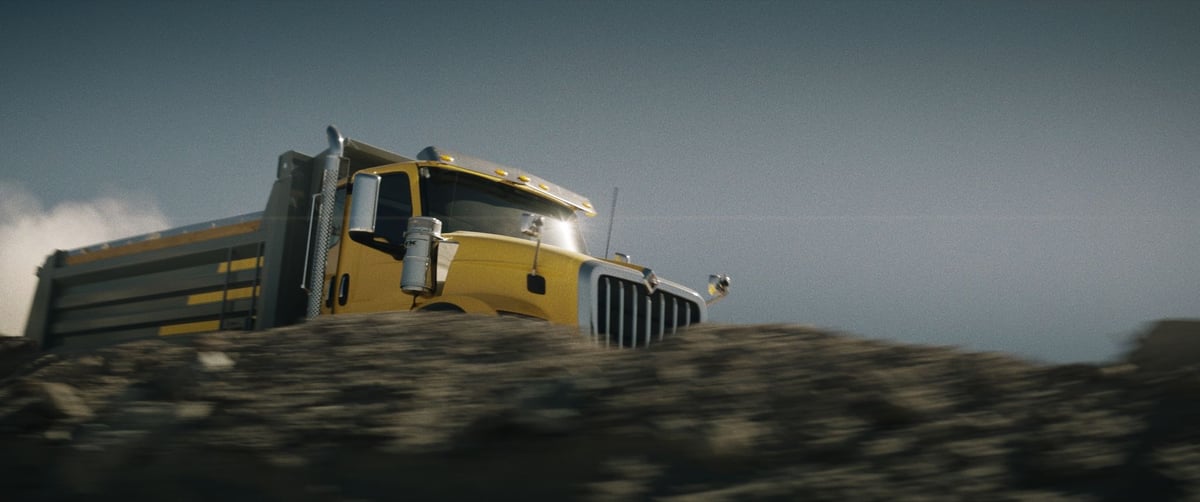 A yellow truck in motion, visible behind a rocky hill