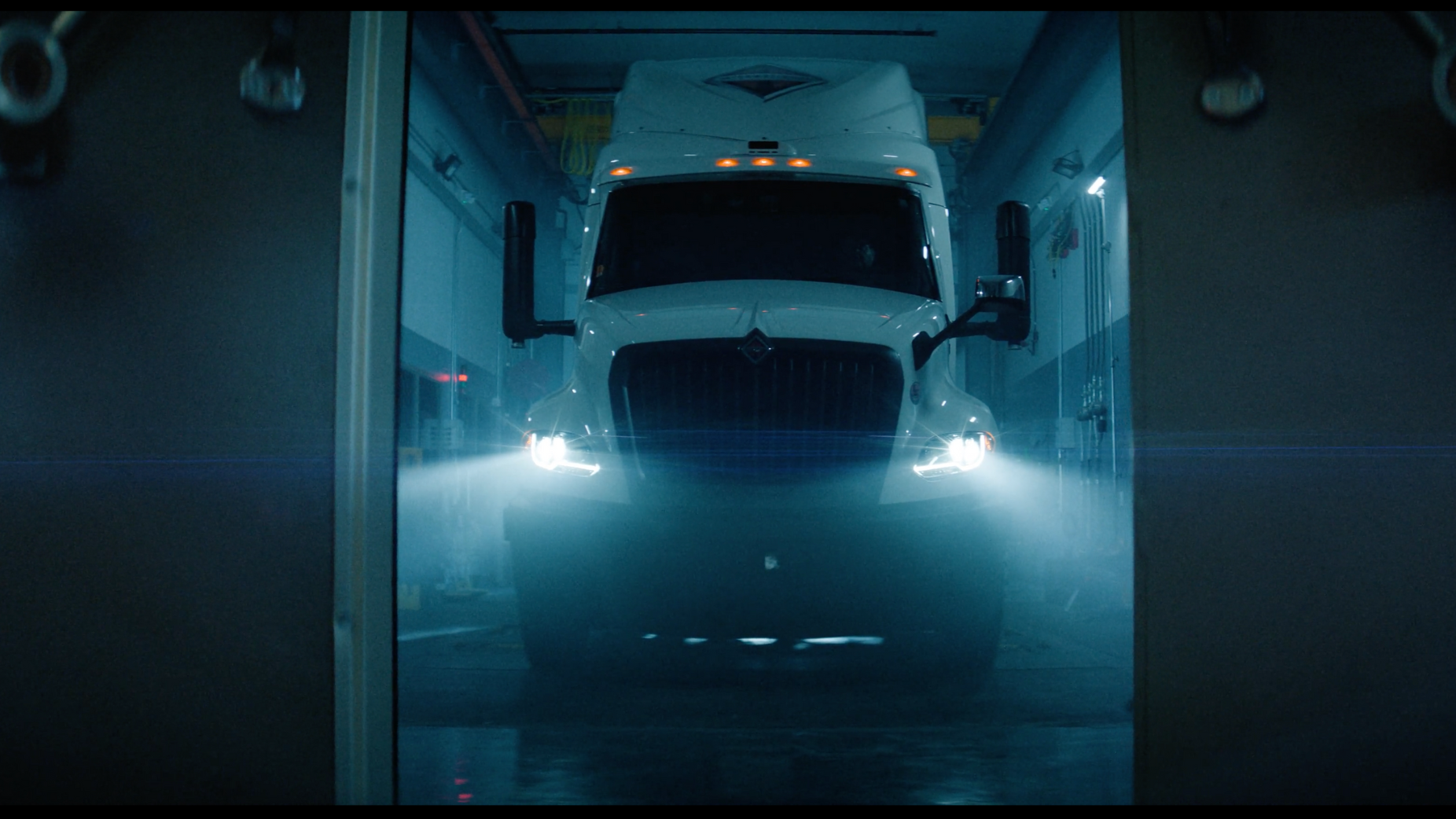 Large white truck with headlights on inside a garage.