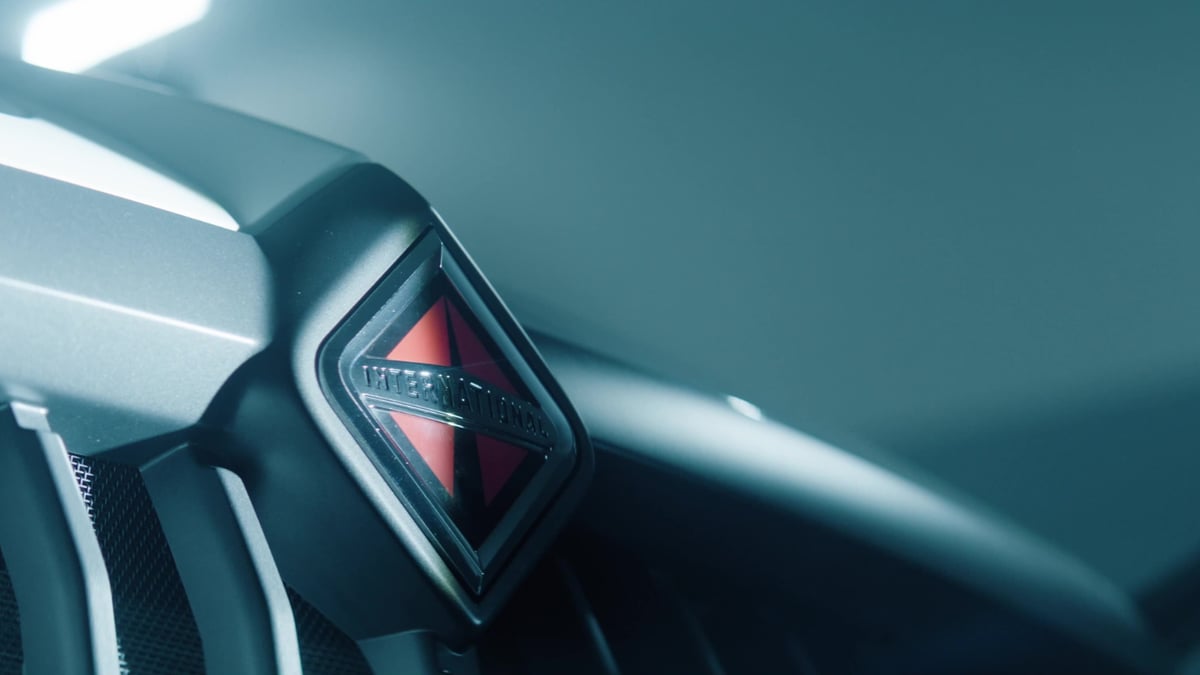 A close-up of a dark truck grille features the red diamond-shaped International Trucks logo with cool blue lighting.