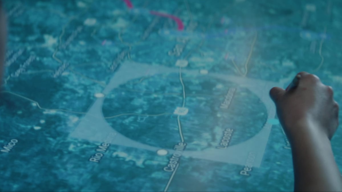 A hand points at a glowing interactive map on a table, with location names .