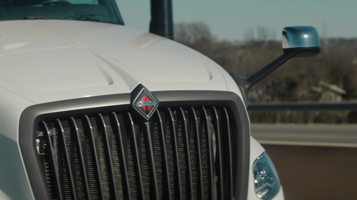 A close-up of the front grille of a white International truck highlights the red diamond logo and vertical chrome grille slats.