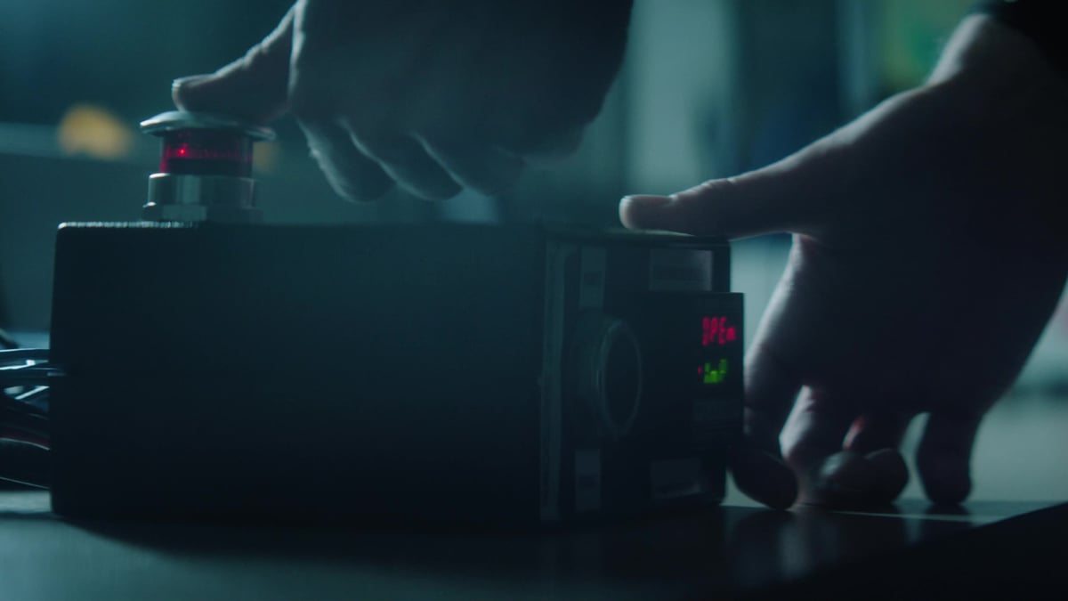 Two hands interact with a compact black electronic device featuring red LED indicators on a dark surface.