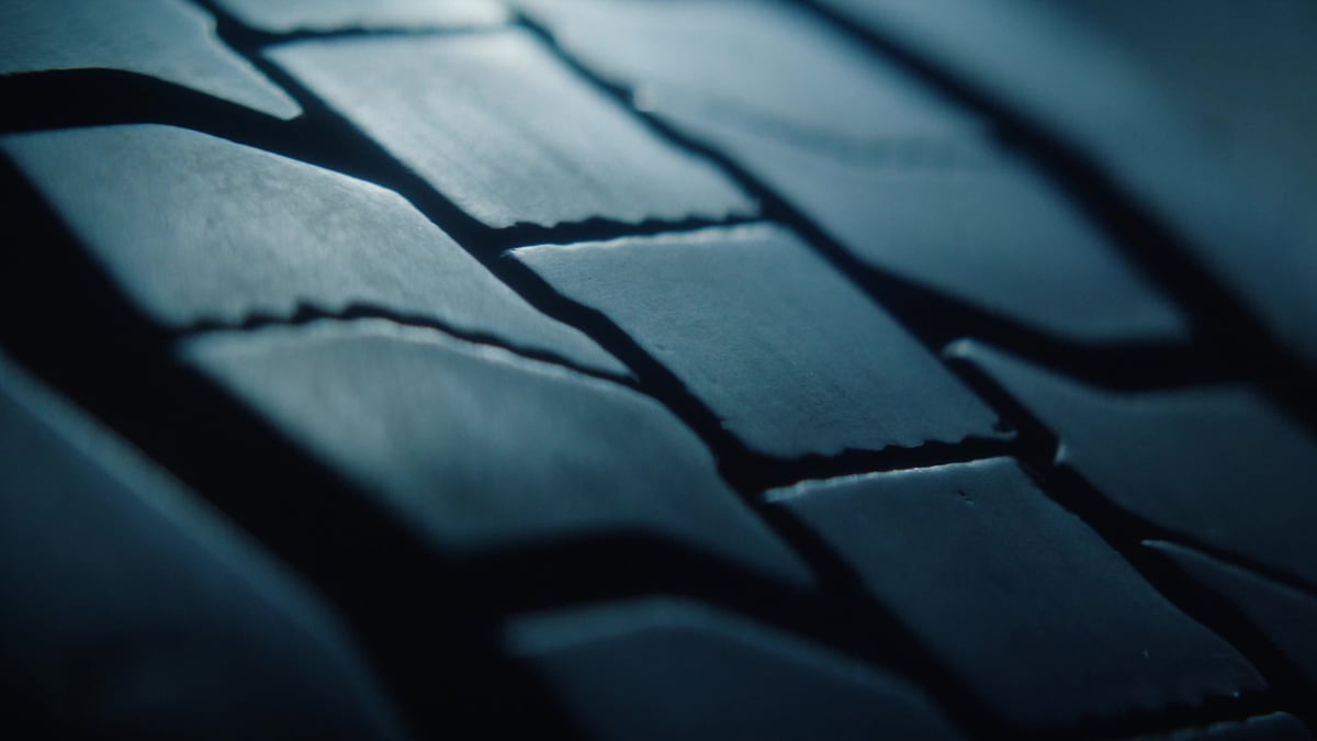 An extreme close-up of a tire's tread pattern reveals deep grooves in a dark, moody blue light.