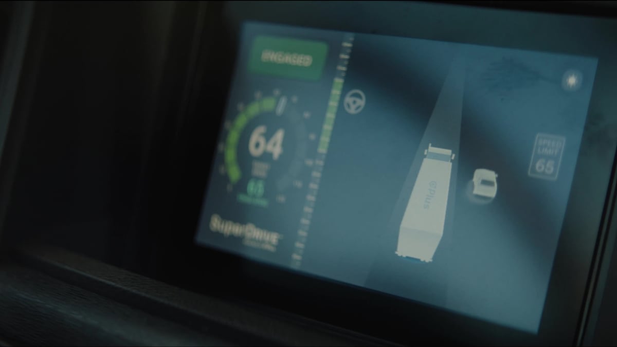 A truck's in-cab display screen shows a "SuperDrive" autonomous driving system engaged at 64 mph with a speed limit of 65.