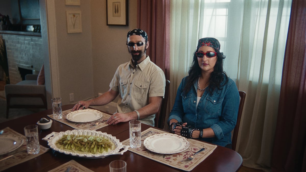 Couple seated at the dining table, wearing sunglasses and headbands, styled like rockstars.