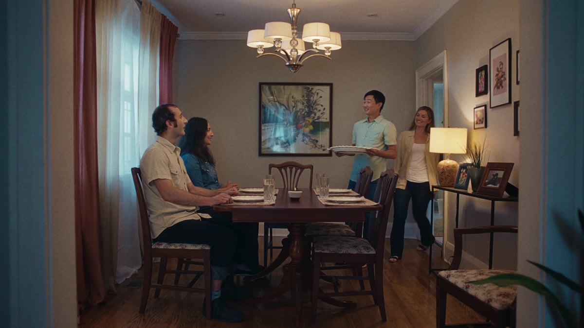 Couple seated at the dining table as another couple approaches with a plate of food.