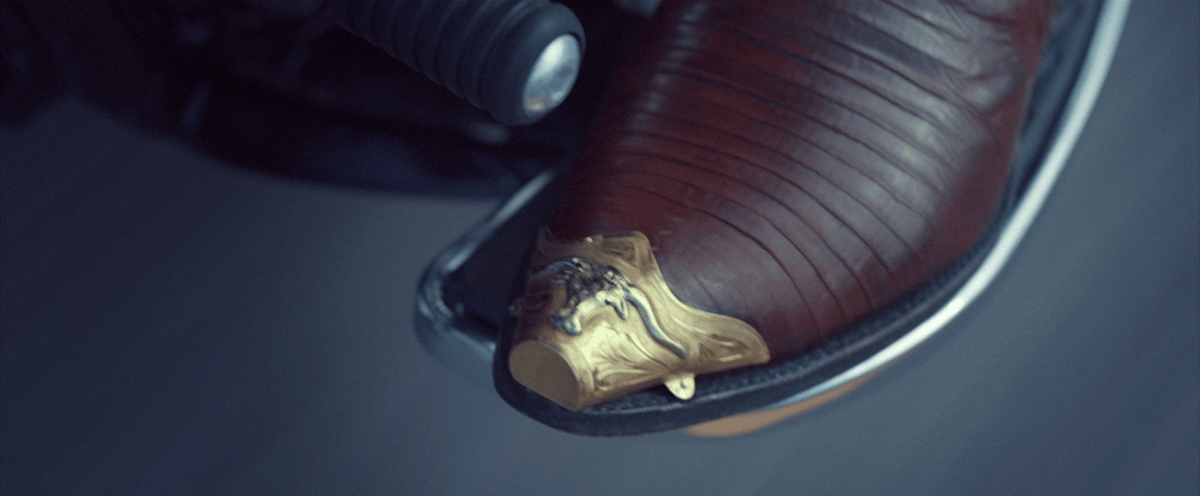 A close-up shot captures the exquisite details of beautiful boots adorned with metal designs at the tips, resting in the motorcycle clutch.