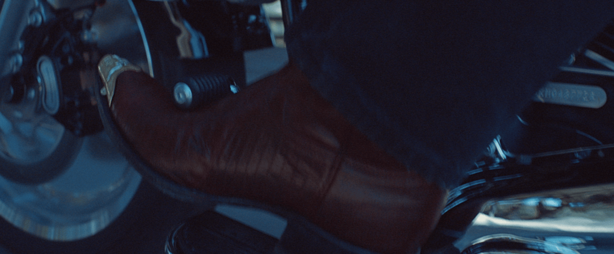 Beautiful boots adorned with metal designs at the tips rest in the motorcycle clutch.