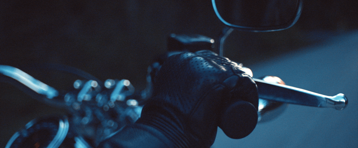 A hand wearing leather gloves grips the motorcycle handlebars while in motion.