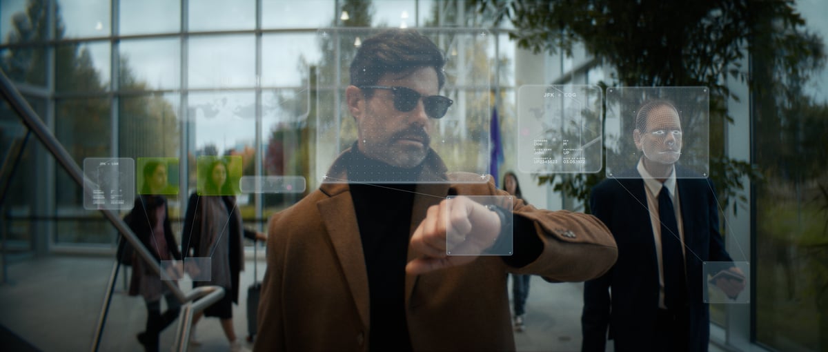 A man wearing sunglasses, glancing at his watch while walking.