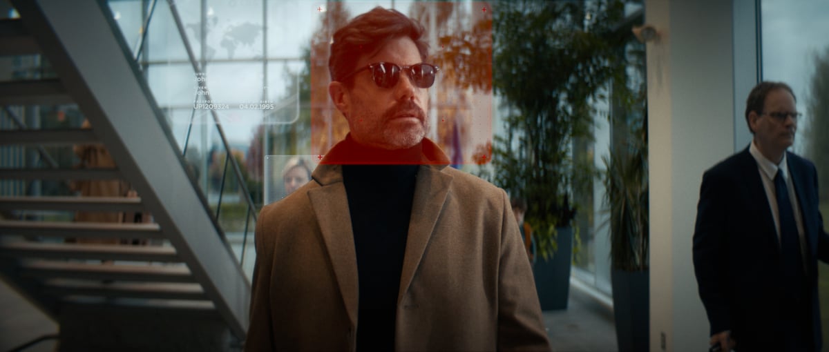 A man wearing sunglasses with a red hologram effect reflecting on his face.