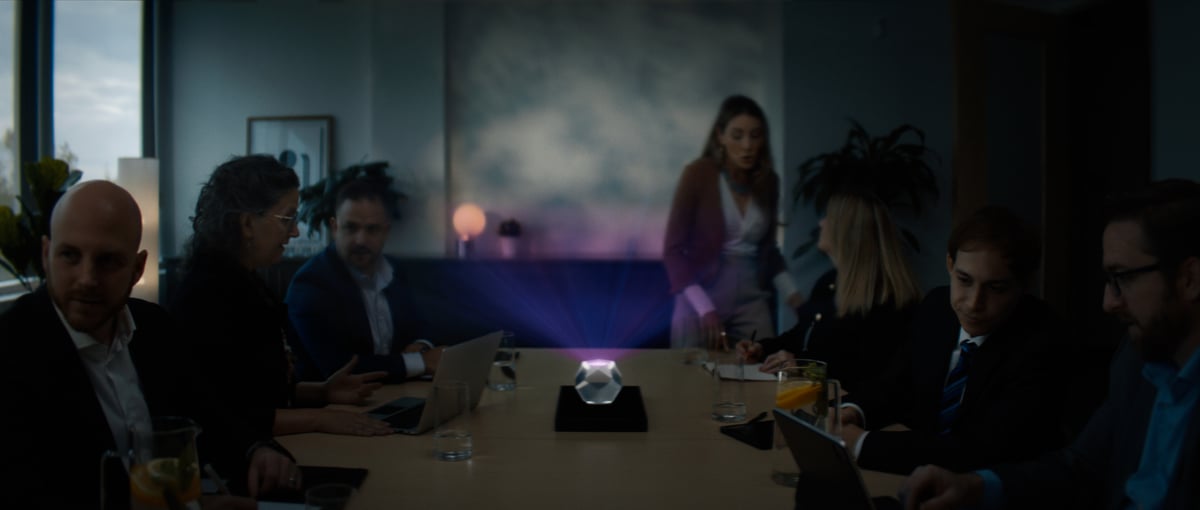 The team assembles around a desk in a meeting.