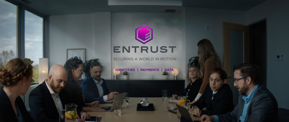 An image depicting a team gathering around a desk for a meeting, featuring the Entrust logo.