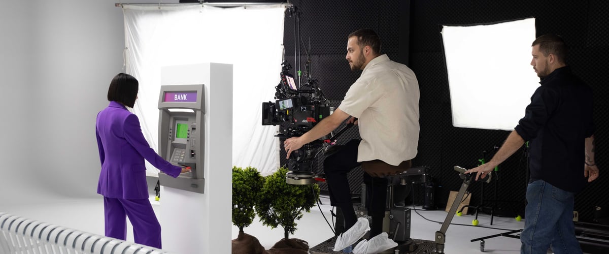 An actress is in the midst of a scene in front of the ATM machine, performing a transaction, while the cameraman carefully captures the moment.