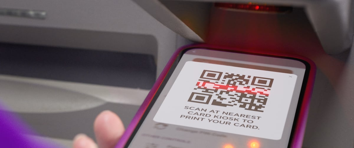 A mobile phone with a displayed QR code is being scanned at the ATM.