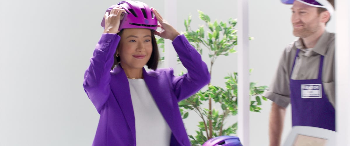 The woman, now wearing her helmet, is getting ready to ride the scooter.