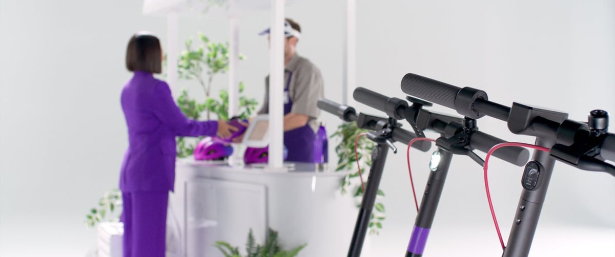 The booth attendant hands the woman a purple helmet after she completes the payment.