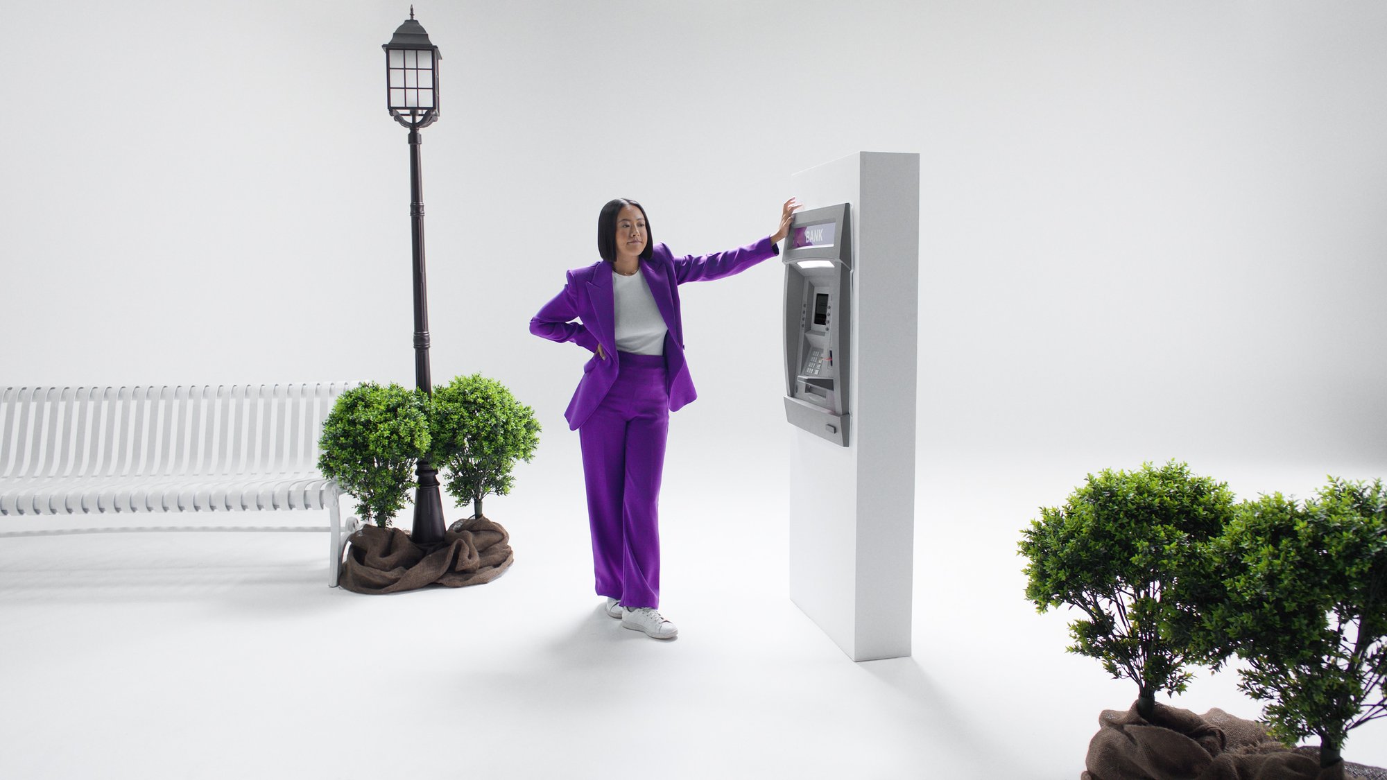 The woman, dressed in a chic purple ensemble, stands by the ATM, patiently waiting for it to respond.