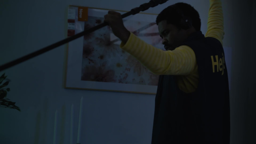 Focused and silent, a crew member in IKEA gear holds a boom mic steady as the set transforms into an overnight recording space.