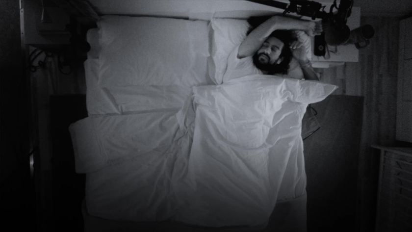 A sleeper stretches mid-dream, framed by soft lighting and concealed microphones in a bedroom that feels too real to be retail.