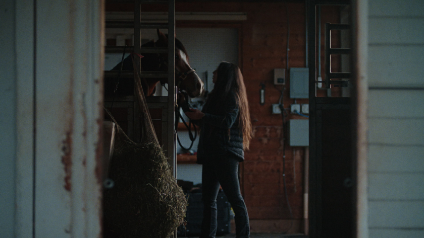 A driver gently prepares her horse inside a dimly lit barn, offering a glimpse into her life off the road.