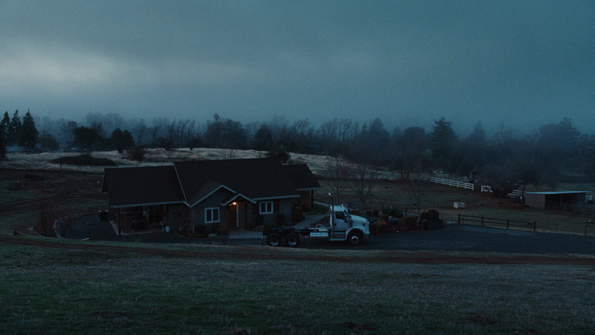 A wide shot of a farmhouse and parked truck under moody pre-dawn skies grounds the story in a rural, lived-in setting.