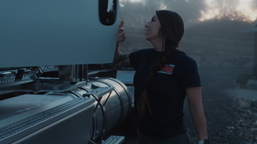 The driver shares a quiet moment with her truck at dawn, framed in soft blue light as the day’s mission begins.