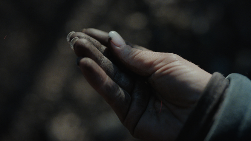 A close-up of a dirt-covered hand captures the raw, physical toll of the work and the intimacy of the moment.