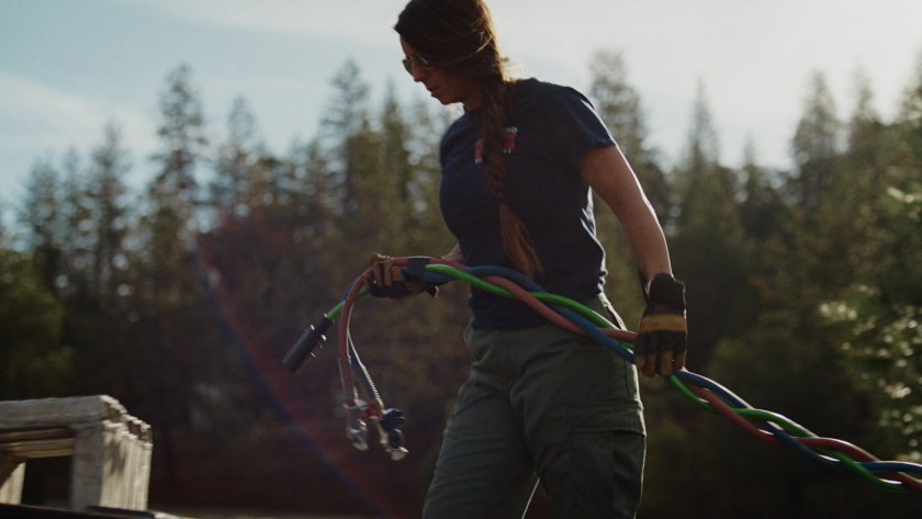 The driver handles vibrant colored cables in golden-hour light, showcasing the hands-on rigging work behind each move.