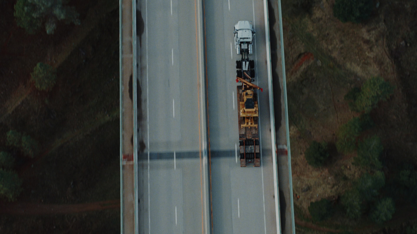 Top-down drone view captures the precision of transport logistics as the truck and heavy equipment slice through open highway.