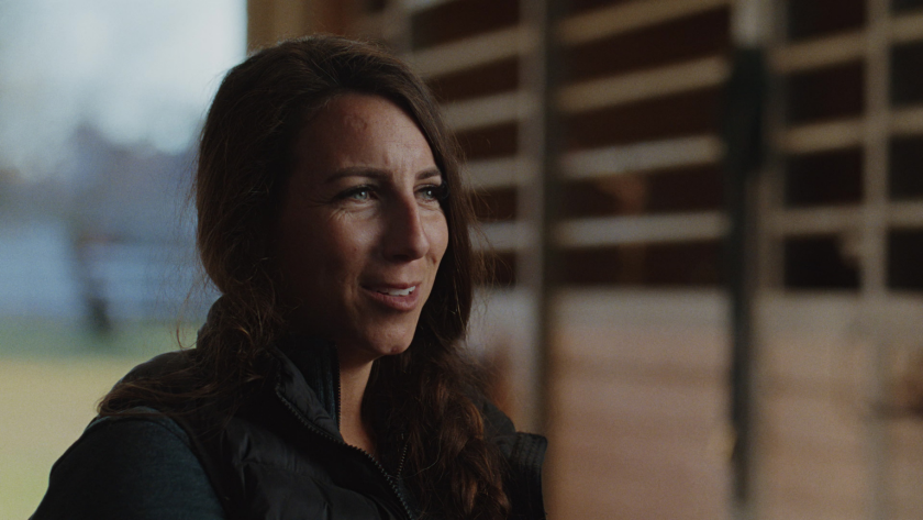 Close-up of the driver in a warmly lit barn, sharing her story with grounded presence and quiet confidence.