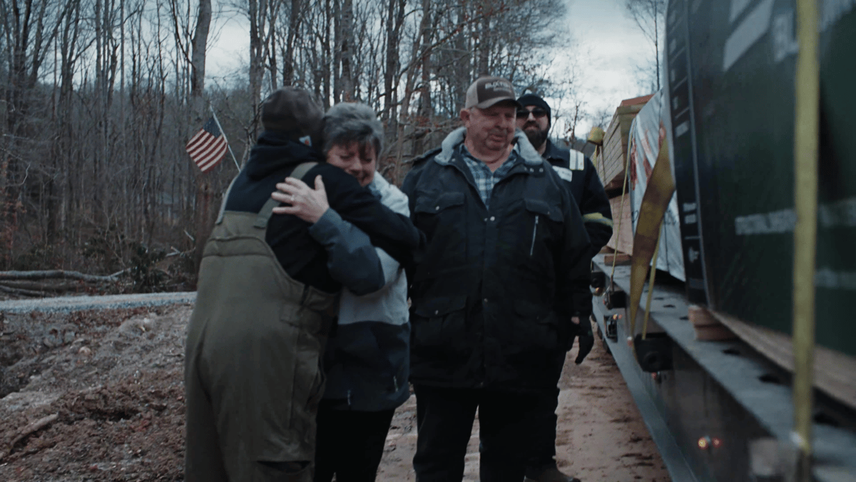 A woman hugs a worker beside a truck loaded with supplies while others look on.