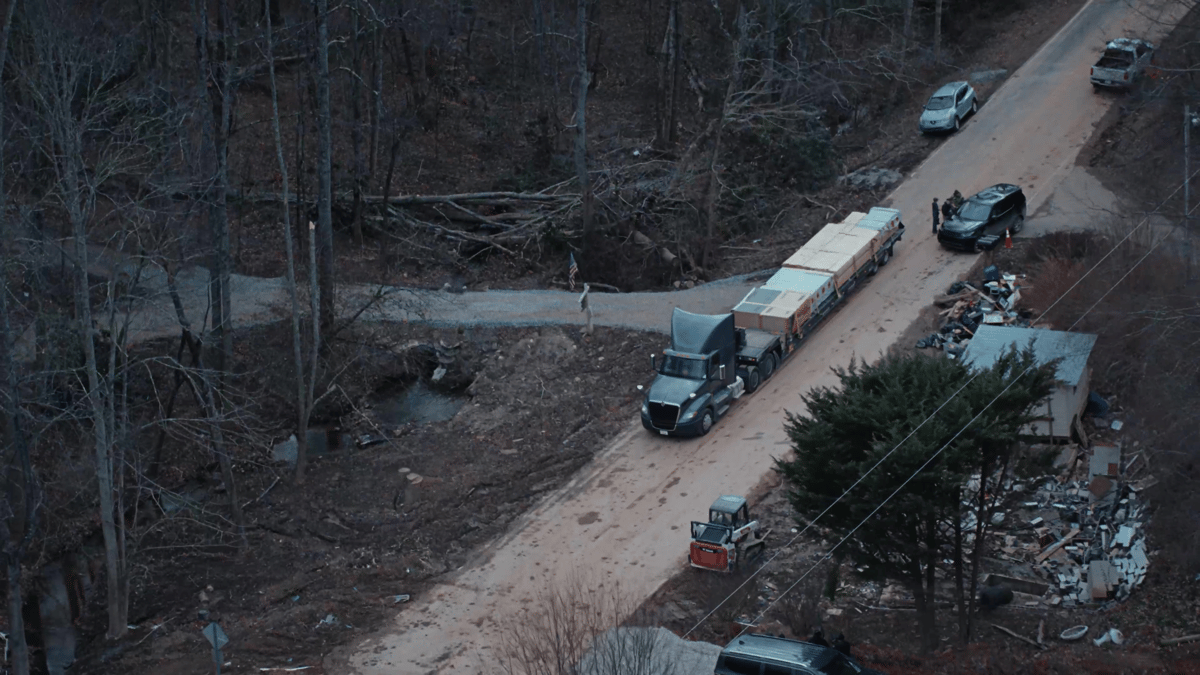 An aerial shot reveals the truck navigating a remote, storm-damaged road, surrounded by debris and downed trees.