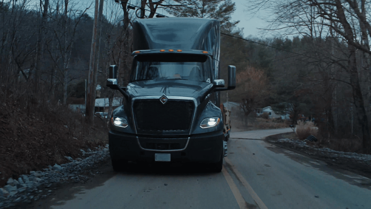 Head-on shot of the truck rolling down a narrow, tree-lined road captures the rugged, real-world path it follows.