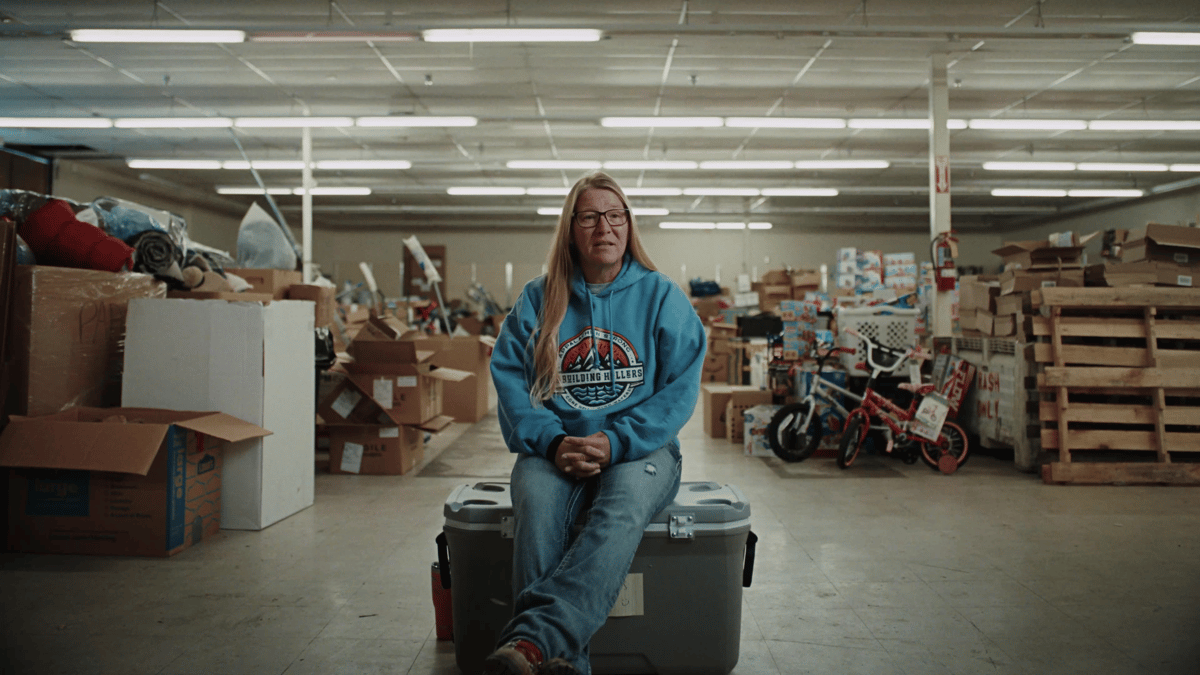 Stephanie Johnson sits among stacks of donated supplies, framed by fluorescent light and surrounded by community effort.