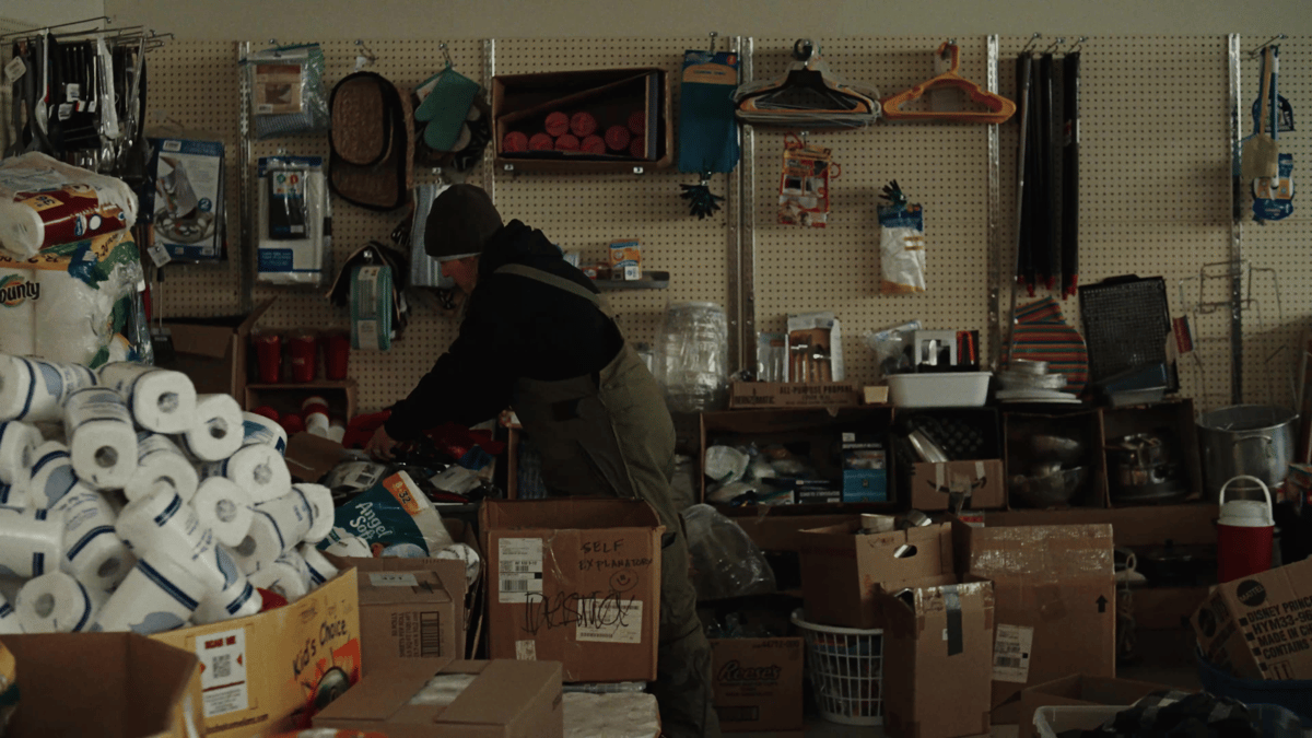 A volunteer sorts through household donations in a cluttered relief depot, underlining the grassroots recovery at work.