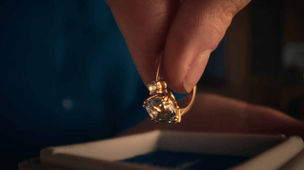 A close-up of a ring held delicately between two fingertips.