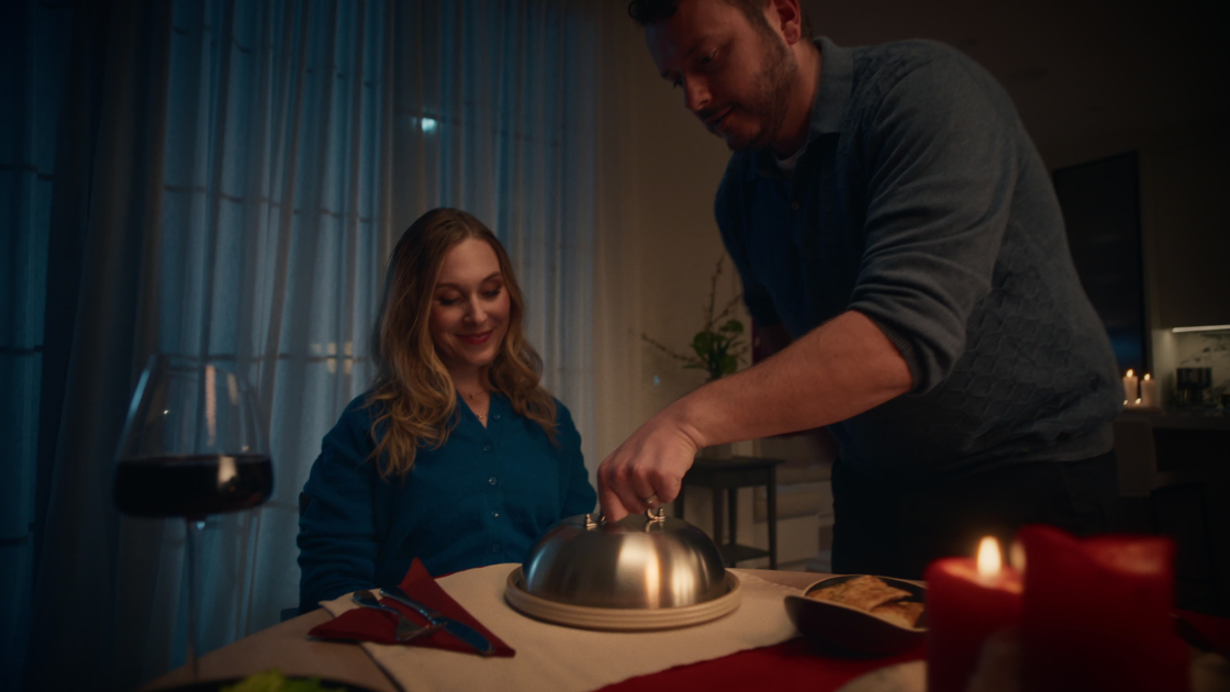 A husband unveiling a dish for his wife, seated at a beautifully set table.