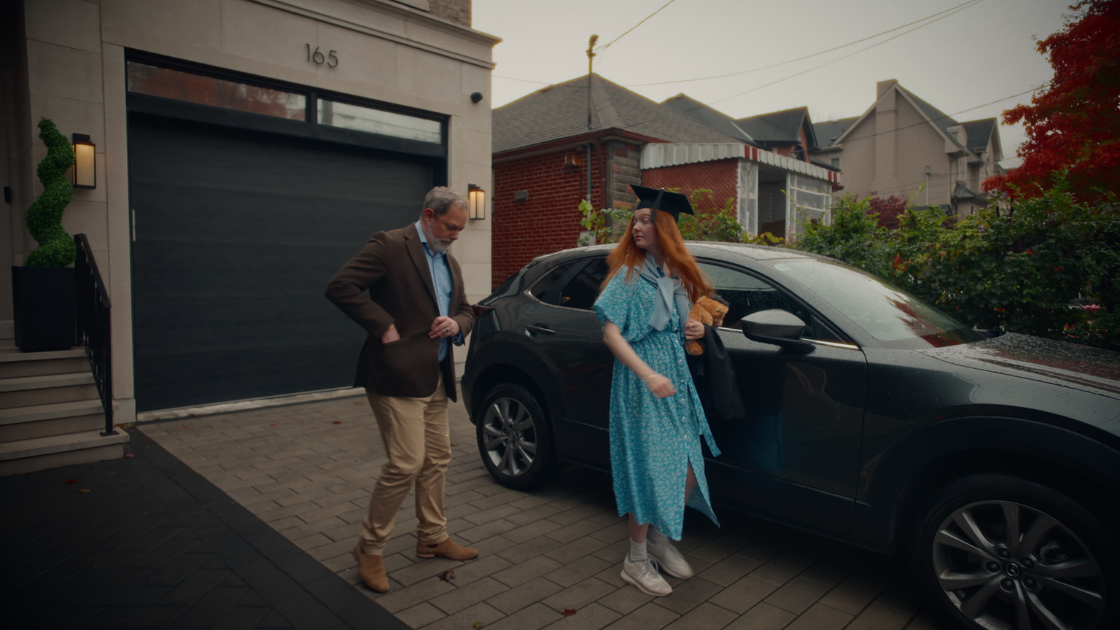A father stopping his daughter as she opens the car door to reveal a surprise.