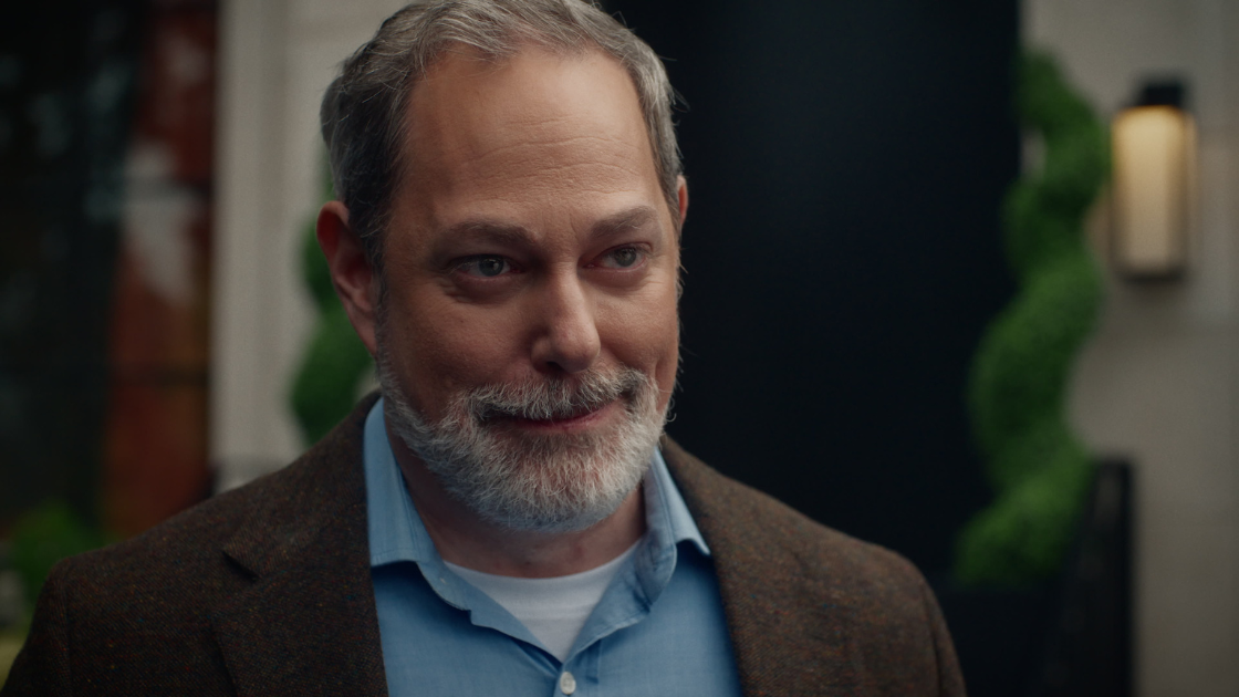 A father proudly watching his daughter's reaction as she opens his gift.