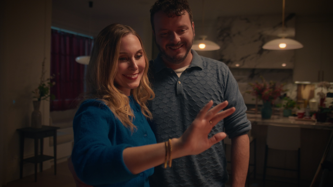 A wife admiring her hand adorned with a ring, with her husband standing lovingly beside her.