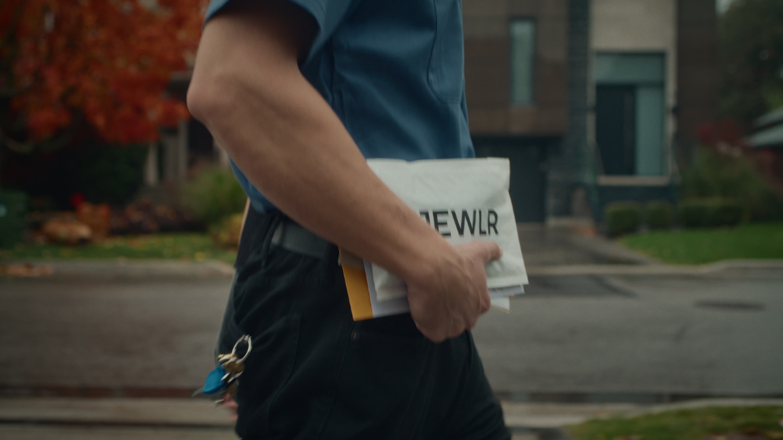 A mailman walking down the street holding a Jewlr package.
