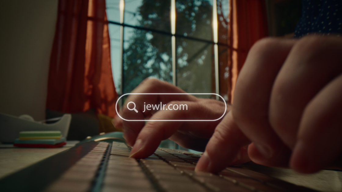 A finger typing on a keyboard with an animated search bar displaying "Jewlr.com."