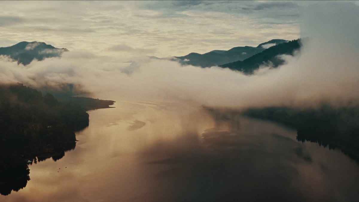 A serene aerial view of a misty river winding between forested mountains in soft morning light.