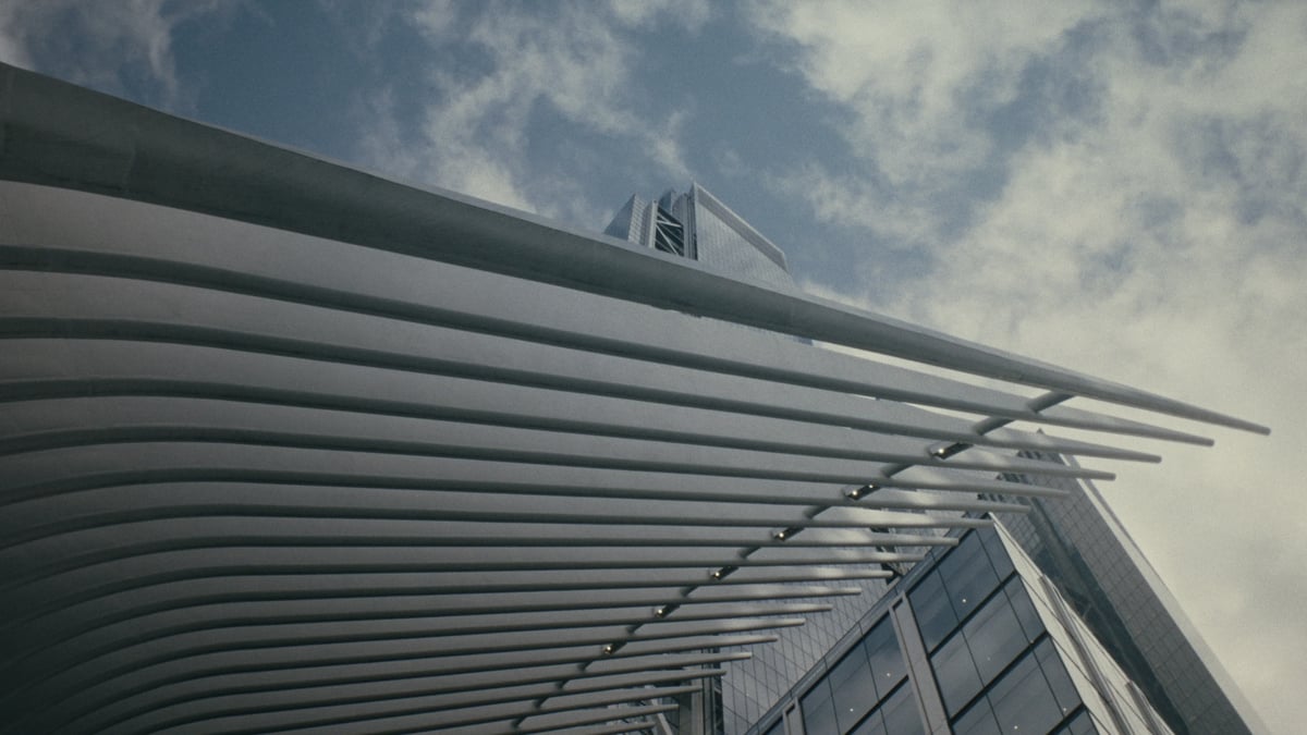 A low-angle architectural shot of the Oculus transit hub's white ribbed structure curving against a partly cloudy sky, with a glass skyscraper rising in the distance.