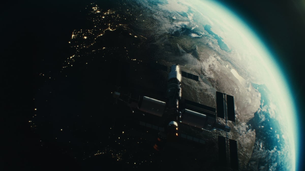 A cinematic view of a satellite or space station orbiting Earth, with the planet's curve and city lights glowing below.