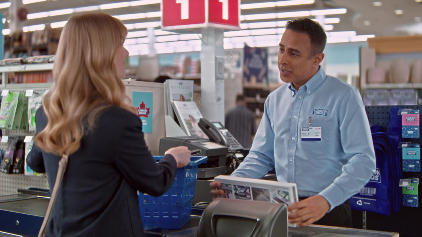 The cashier and customer engage in conversation as a blue basket of items sits on the counter.