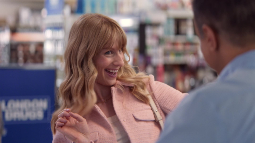 A smiling customer in a pink jacket gestures playfully toward the cashier.