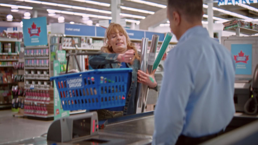 A customer awkwardly juggles large rolls of wrapping paper at the checkout counter.